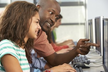 Teacher Helping Students Working At Computers In Classroom