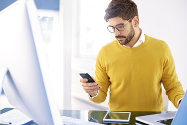 Handsome businessman sitting in the office and text messaging on his cell phone